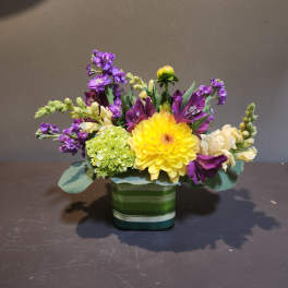 Yellow dahlia bouquet with purple and white flowers in a striped glass vase