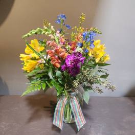 Colorful mixed bouquet in a glass vase with a rainbow ribbon
