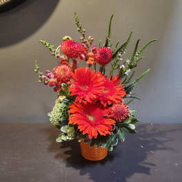 Orange gerbera daisies and pink blooms in a small vase