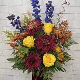 Mixed bouquet in a burgundy vase with yellow roses and blue delphinium