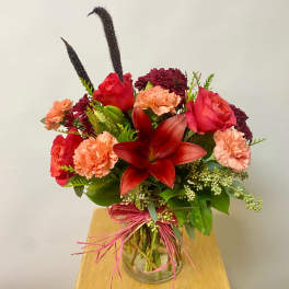 Bouquet of red roses, carnations, and a red lily in a glass vase