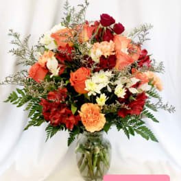 Mixed bouquet of red, peach, and white flowers in a glass vase
