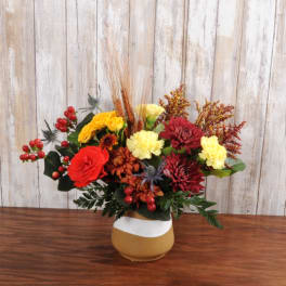 Autumn bouquet of red, yellow, and orange flowers with berries in a two-tone ceramic vase on a wooden table