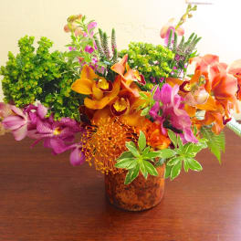 Mixed orchid arrangement in a brown vase with orange and purple blooms