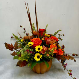 Autumn floral arrangement in a pumpkin-shaped container with orange and yellow blooms