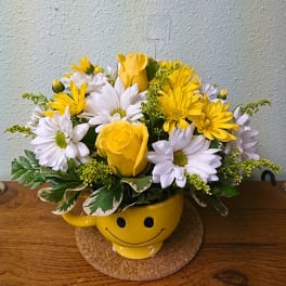 Yellow and white flower arrangement in a smiley-face mug