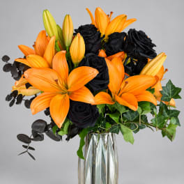 Orange lilies and black roses in a clear glass vase