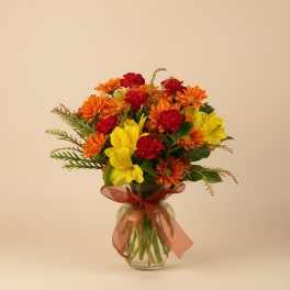 Bouquet of orange, yellow, and red flowers in a glass vase with a ribbon