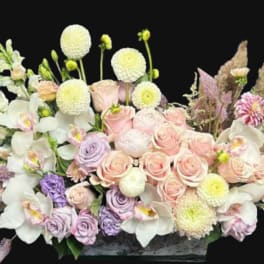 Pastel floral arrangement with roses, orchids, and round white blooms in a low container