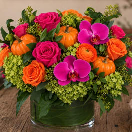Pink and orange floral arrangement with small pumpkins in a glass vase