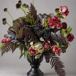 Dark floral arrangement in a black pedestal vase with burgundy blooms and berries