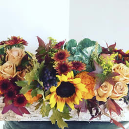 Autumn floral arrangement with sunflowers, roses, and chrysanthemums in a low container