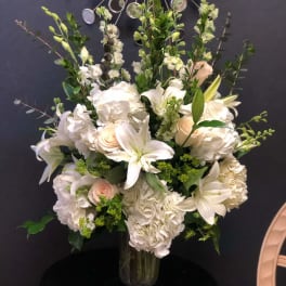 White floral arrangement in a glass vase with lilies, roses, and hydrangeas