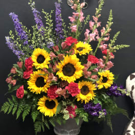 Mixed bouquet with sunflowers, pink carnations, and purple spikes in a gray vase