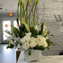 Tall white arrangement with calla lilies, roses, orchids and curly branches in a square white vase