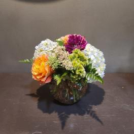 Mixed flower arrangement in a round glass vase with orange, purple, and white blooms
