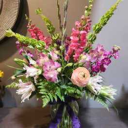 Mixed pink and white flowers in a glass vase with a purple ribbon