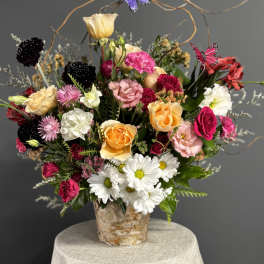 Mixed bouquet of roses, daisies, and carnations in a birch-style container