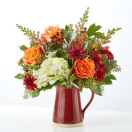 Orange and burgundy flowers arranged in a red pitcher vase