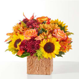 Autumn bouquet of sunflowers, roses, and mums in a leaf-patterned vase