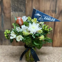 White flowers in a glass vase with a Philadelphia Eagles pennant and football decoration