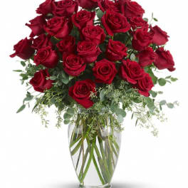 Red roses arranged in a clear glass vase with greenery