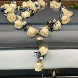 White rose heart-shaped casket spray with blue accents and a hanging rosary