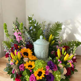 Colorful floral wreath around a pale urn with sunflowers, roses, lilies, and hydrangeas