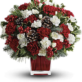 Red and white floral arrangement in a square glass vase with pinecones and berries