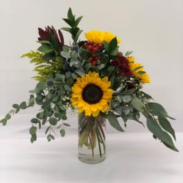 Sunflower arrangement in a clear glass vase with mixed greenery and red berries