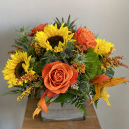 Orange roses and yellow sunflowers in a square container
