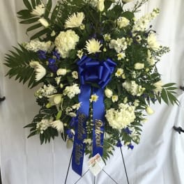 Large white floral standing wreath with blue ribbon on an easel