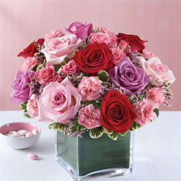 Bouquet of red, pink, and lavender roses in a square glass vase