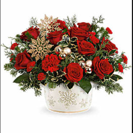 Red roses arranged in a white snowflake vase with holiday accents