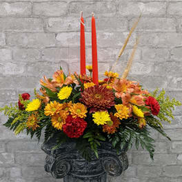 Autumn floral arrangement with red candles in a dark pedestal vase