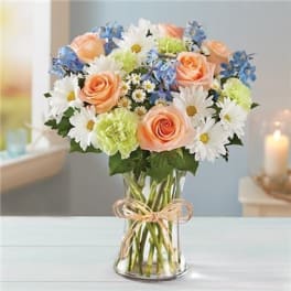 Bouquet of peach roses, white daisies, and blue flowers in a glass vase