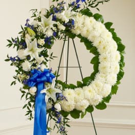 White floral funeral wreath with blue ribbon on a stand