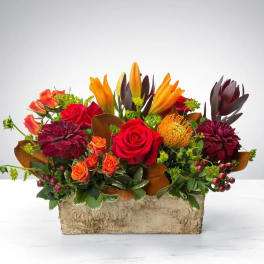 Mixed bouquet with red roses, orange lilies, and burgundy blooms in a rectangular container