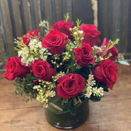 Red roses arranged in a dark glass vase with small white filler flowers