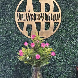 Pink rose bouquet in a clear vase with a wooden monogram sign behind it
