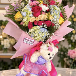Mixed bouquet in pink wrap with a teddy bear attached at the base