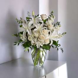 White lilies and cream roses arranged in a clear glass vase