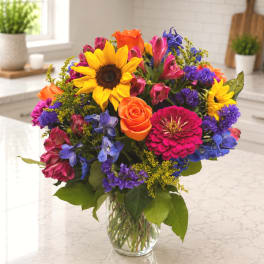 Colorful mixed bouquet with sunflowers, roses, and a clear glass vase