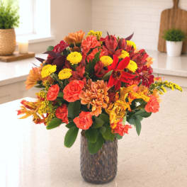 Mixed autumn bouquet in a textured glass vase with red, orange, and yellow blooms