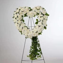 White rose heart wreath on a black easel with trailing greenery