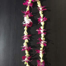 Two purple and white flower leis on a dark surface