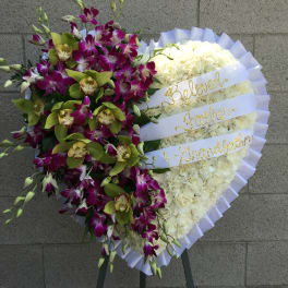 Heart-shaped floral tribute with white flowers and purple orchids on a stand