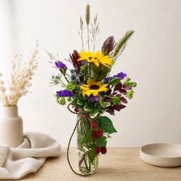 Mixed bouquet with yellow sunflowers and purple flowers in a clear glass vase