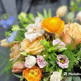Handheld bouquet of peach roses, orange ranunculus, and pastel blooms against a dark jacket.