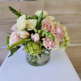 Low arrangement of pale pink roses, white roses, tulips, and green hydrangea in a clear glass vase